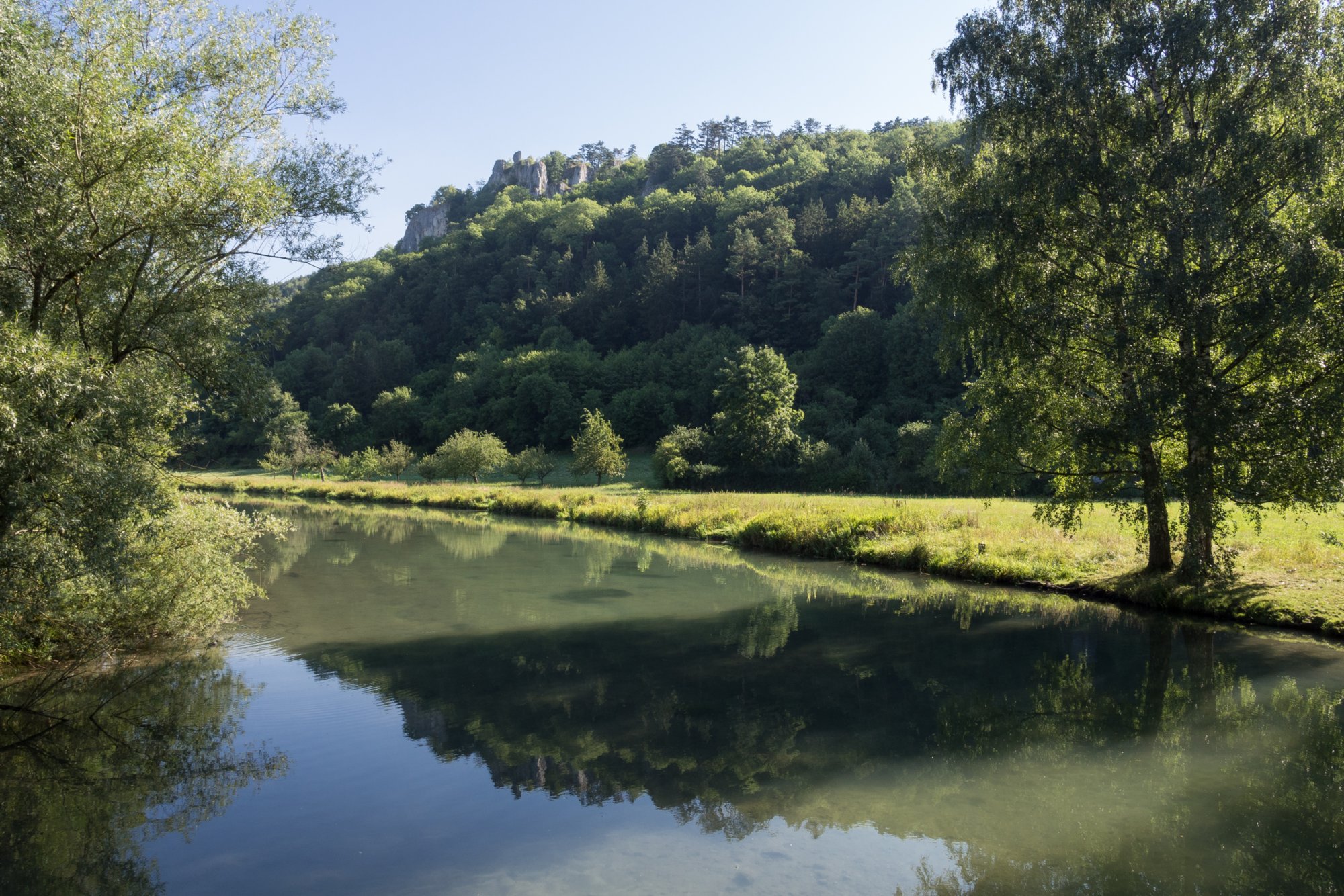 An der Blau. Blick zum Rusenschloss. Wanderung von Blaubeuren Bahnhof zum Rusenschloss. Von dort über den Knoblauchfelsen zum Blaufelsen. Hinunter zur B28. Diese überquerend Aufstieg auf Teerweg bis zur Steigziegelhütte, da Abzweig nach links zum Landeplatz Seißen nicht gefunden. Entlang am Waldrand zur Wegmarkierung. Dieser folgend zur Günzelburg. Von dort zum Felsenlabyrinth und zur Küssenden Sau. Abstiefg zum Bahnhof. Mit dem Auto zum Blautopf.